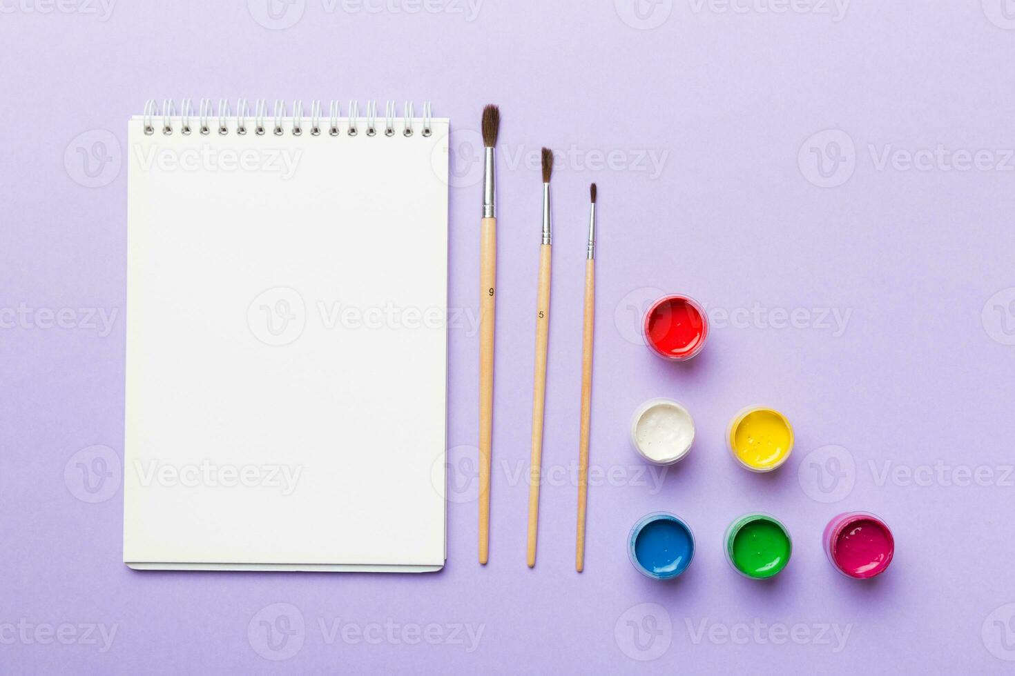 Album pages and paints, pencils, brush on a colored background. Top view with empty space. workplace for creativity. home teaching concept drawing photo