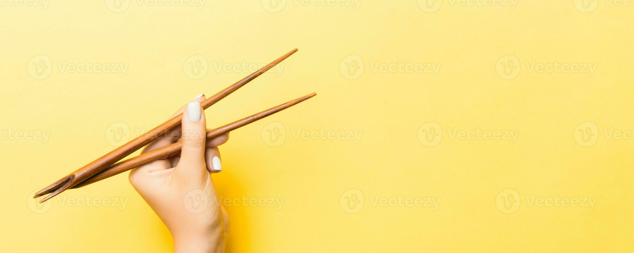 palillos de madera en mano femenina sobre fondo amarillo con espacio vacío para tu idea. concepto de comida sabrosa foto