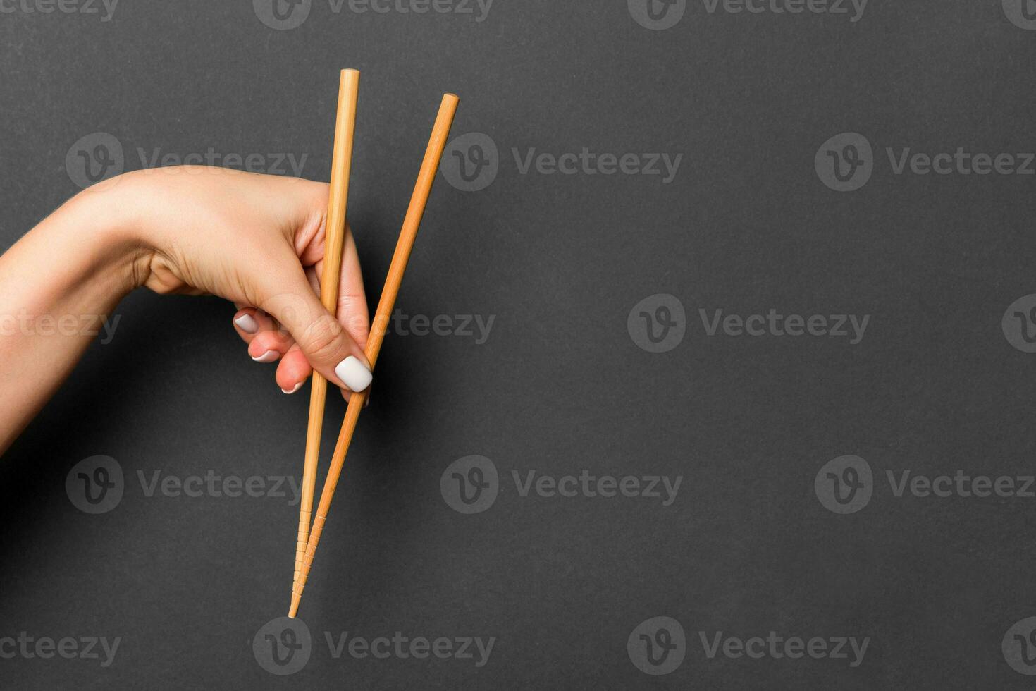 Wooden chopsticks holded with female hands on black background. Ready for eating concepts with empty space photo