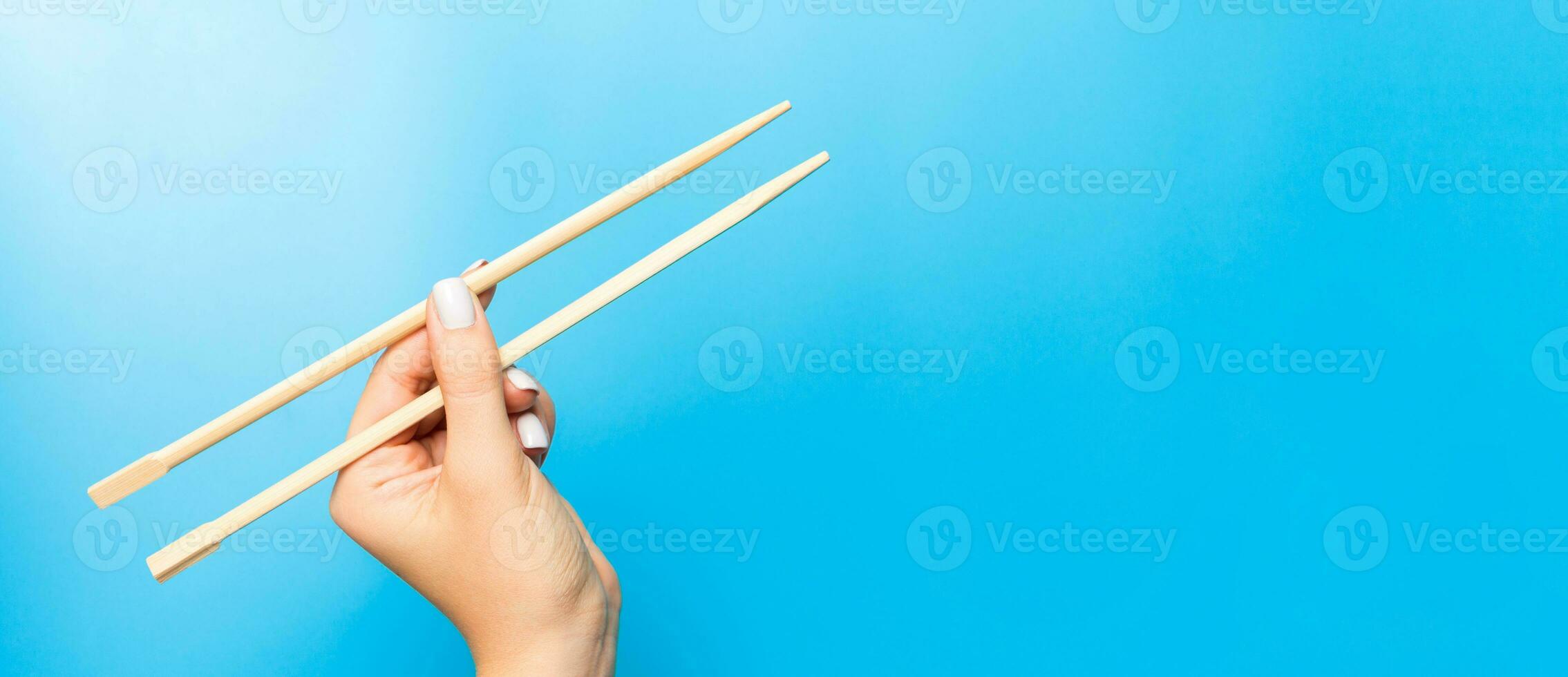 Wooden chopsticks holded with female hands on blue background. Ready for eating concepts with empty space photo