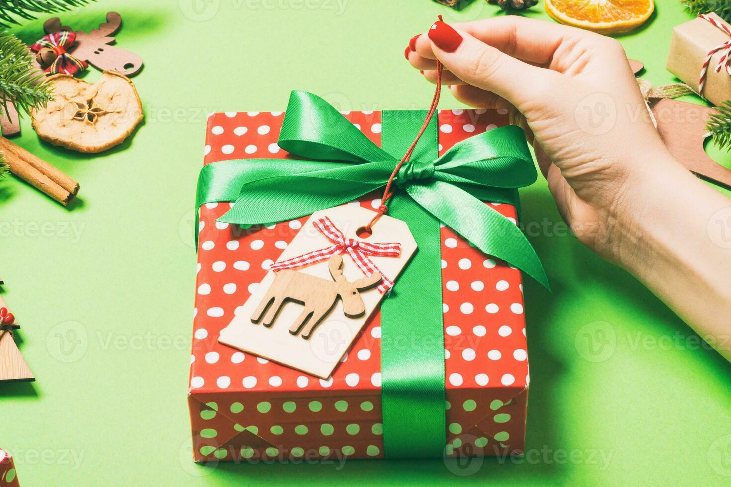 Top view of female hands holding a Christmas present on festive green background. Fir tree and holiday decorations. New Year holiday concept photo