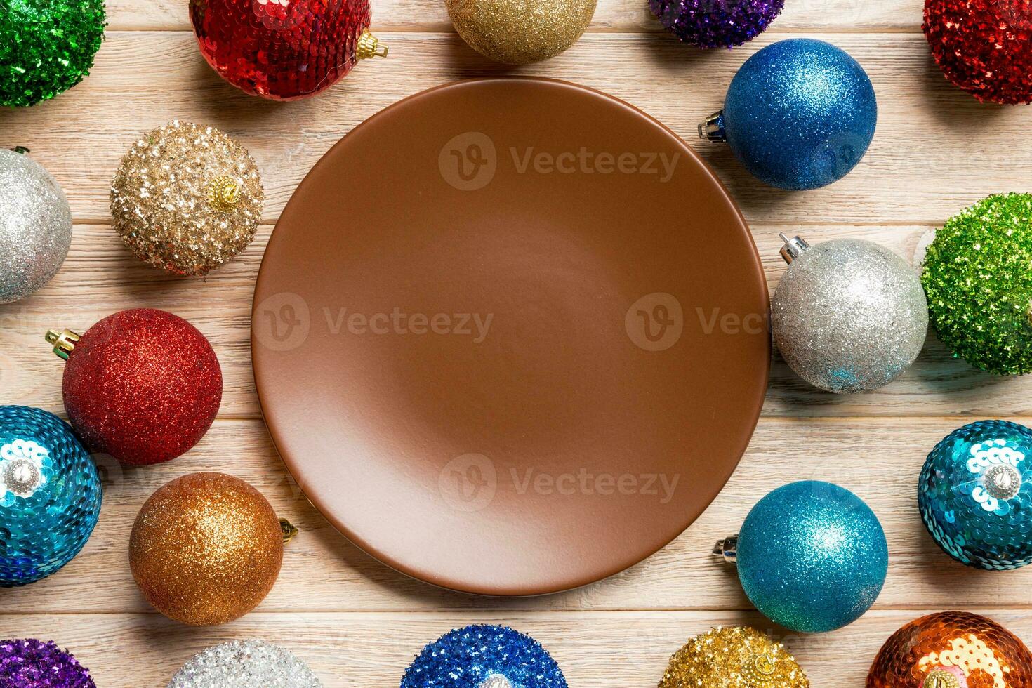 Top view of empty plate surrounded with colorful baubles on wooden background. New Year decorations. Christmas Eve concept photo