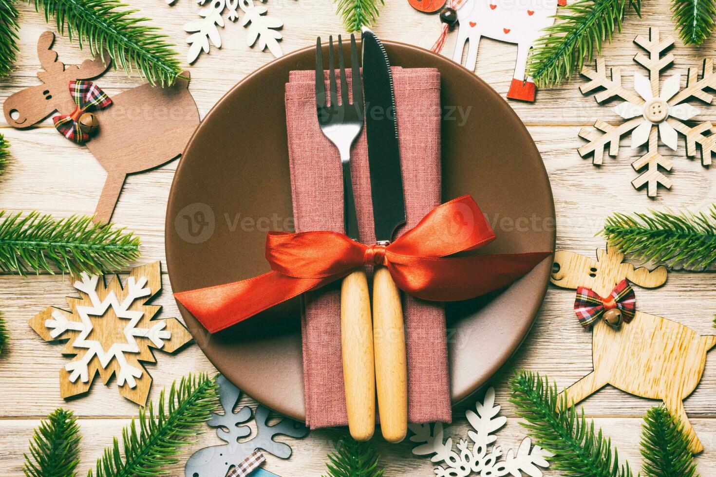 Top view of cutlery and plate on festive wooden background. New Year family dinner concept. Fir tree and Christmas decorations photo