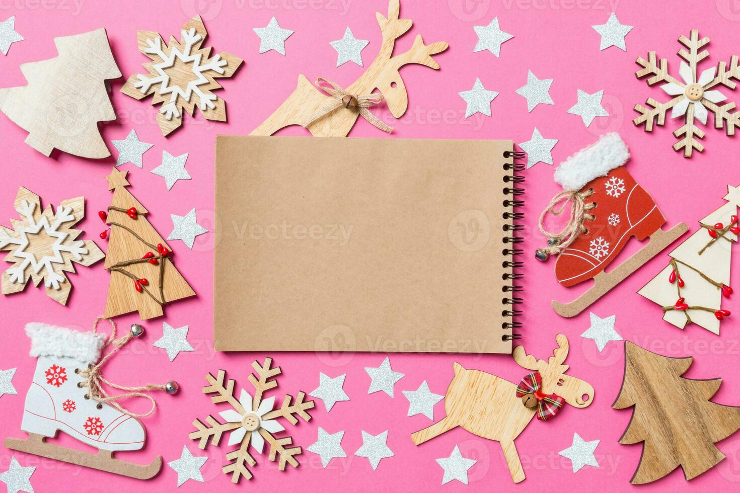 Top view of notebook, pink background decorated with festive toys and Christmas symbols reindeers and New Year trees. Holiday concept photo