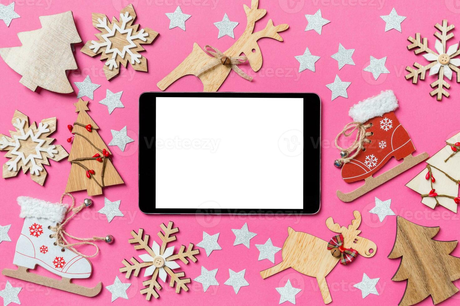 Top view of digital tablet, pink background decorated with festive toys and Christmas symbols reindeers and New Year trees. Holiday concept photo