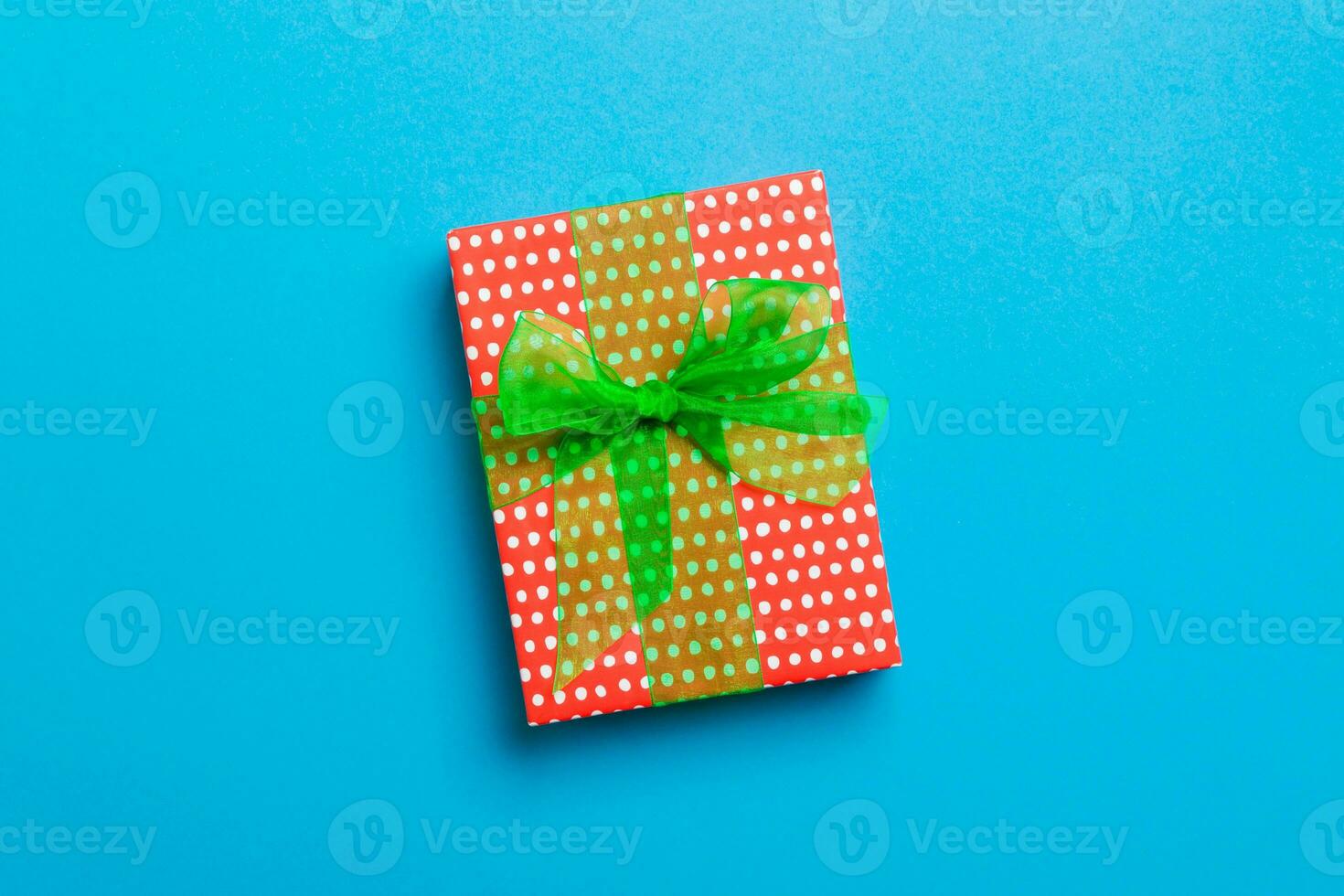 wrapped Christmas or other holiday handmade present in paper with green ribbon on blue background. Present box, decoration of gift on colored table, top view with copy space photo