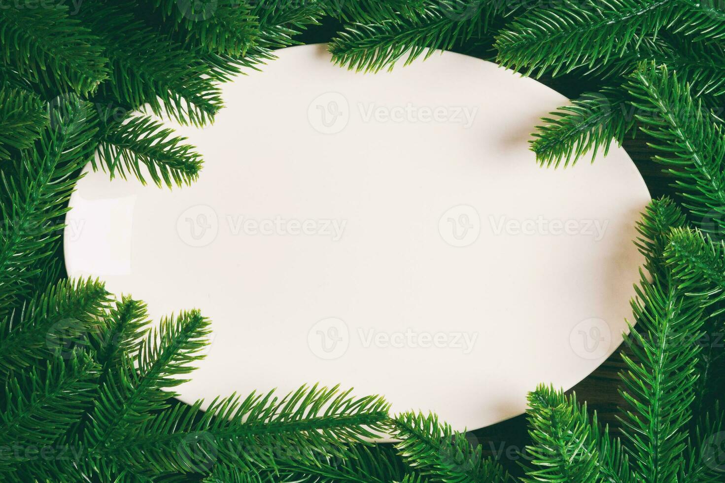 Top view of white plate surrounded with fir tree branches. Christmas dinner concept with copy space photo