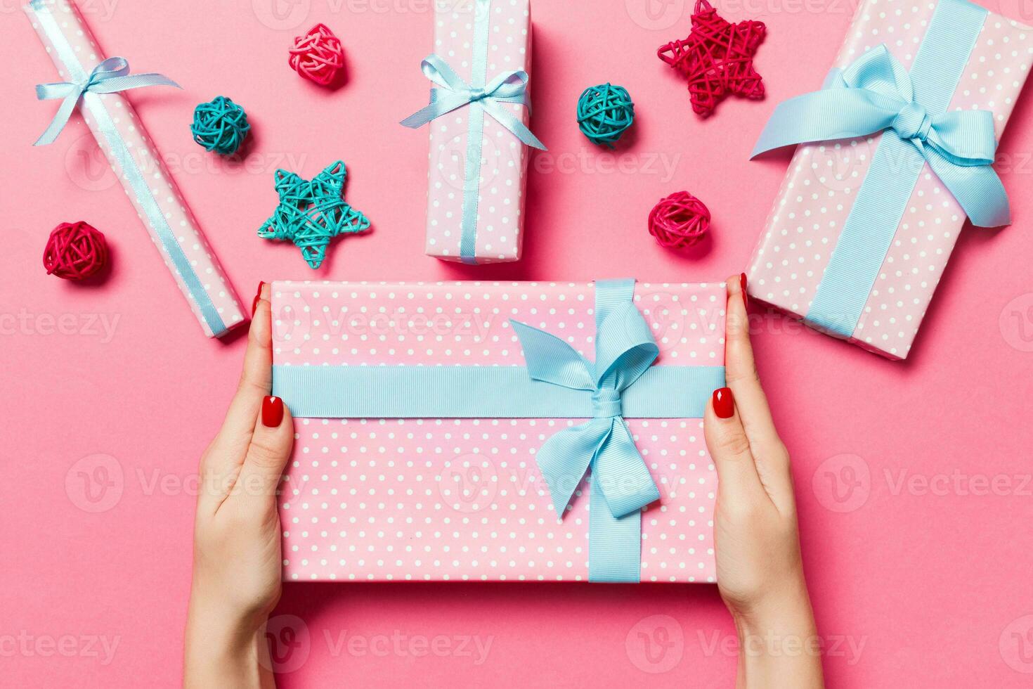 Top view of female hands holding a Christmas present on festive pink background. Holiday decorations, toys and balls. New Year holiday concept photo