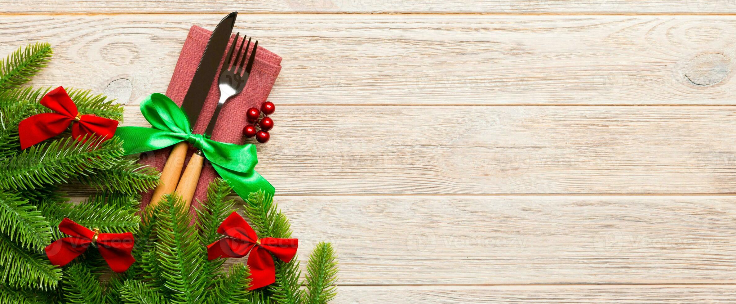 Top view of christmas decorations on wooden background. Fork and knife on napkin tied up with ribbon and empty space for your design. New year pattern concept photo