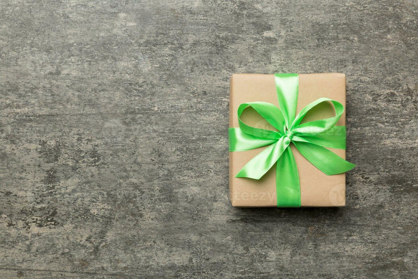 Holiday gift box wrapped in craft paper with colored bow on table background. Top view, flat lay, copy space photo
