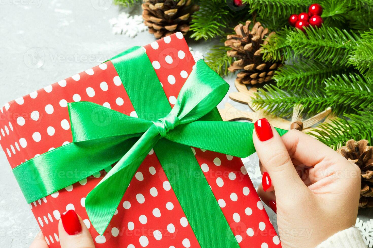 Top view of a woman holding a gift box in her hands on festive cement background. Fir tree and Christmas decorations. New year time concept photo