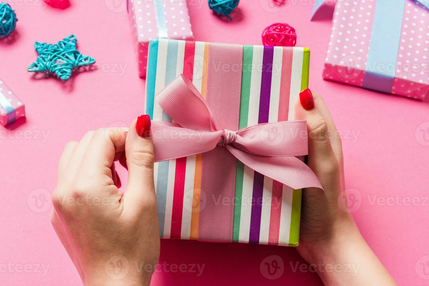 Top view of female hands holding a Christmas present on festive pink background. Holiday decorations, toys and balls. New Year holiday concept photo