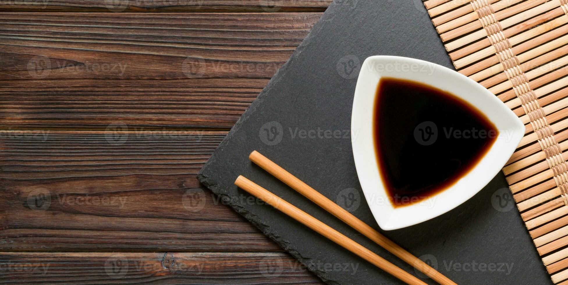 Chopsticks and soy sauce on black stone plate, wooden background with copy space photo