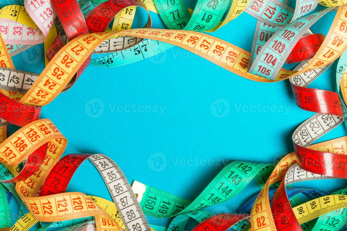 Top view of frame made of heap of colorful measure tapes on turquoise background. Keeping fit concept with empty space for your design photo