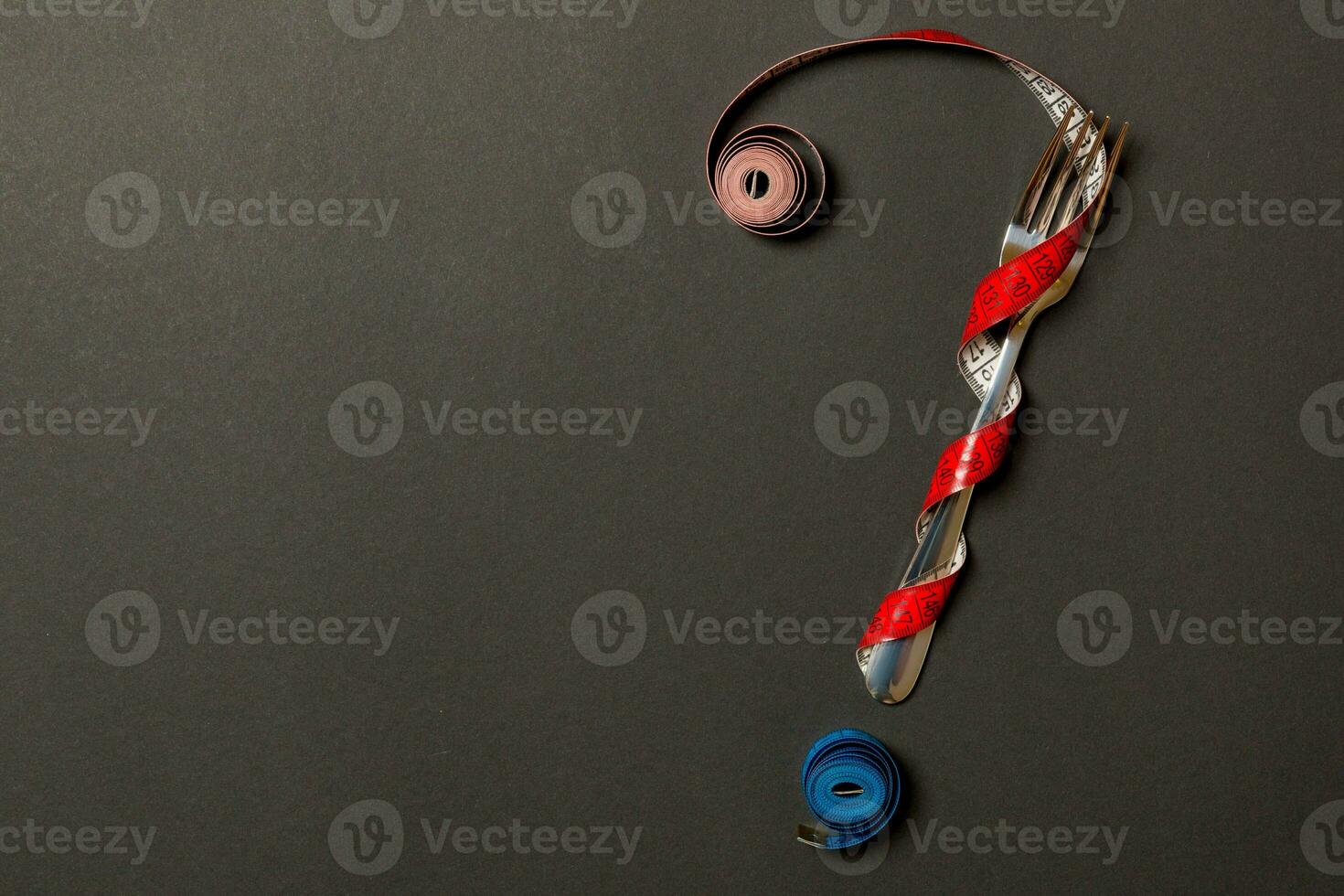 Top view of question mark made of fork and measuring tape on black background. Diet concept with copy space photo