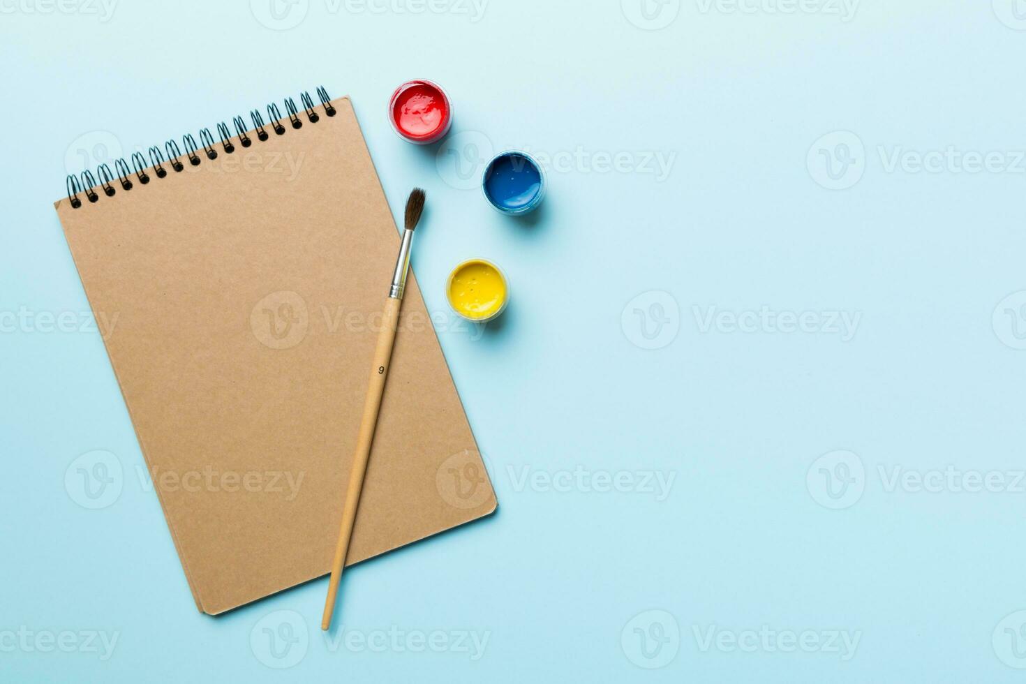 Album pages and paints, pencils, brush on a colored background. Top view with empty space. workplace for creativity. home teaching concept drawing photo