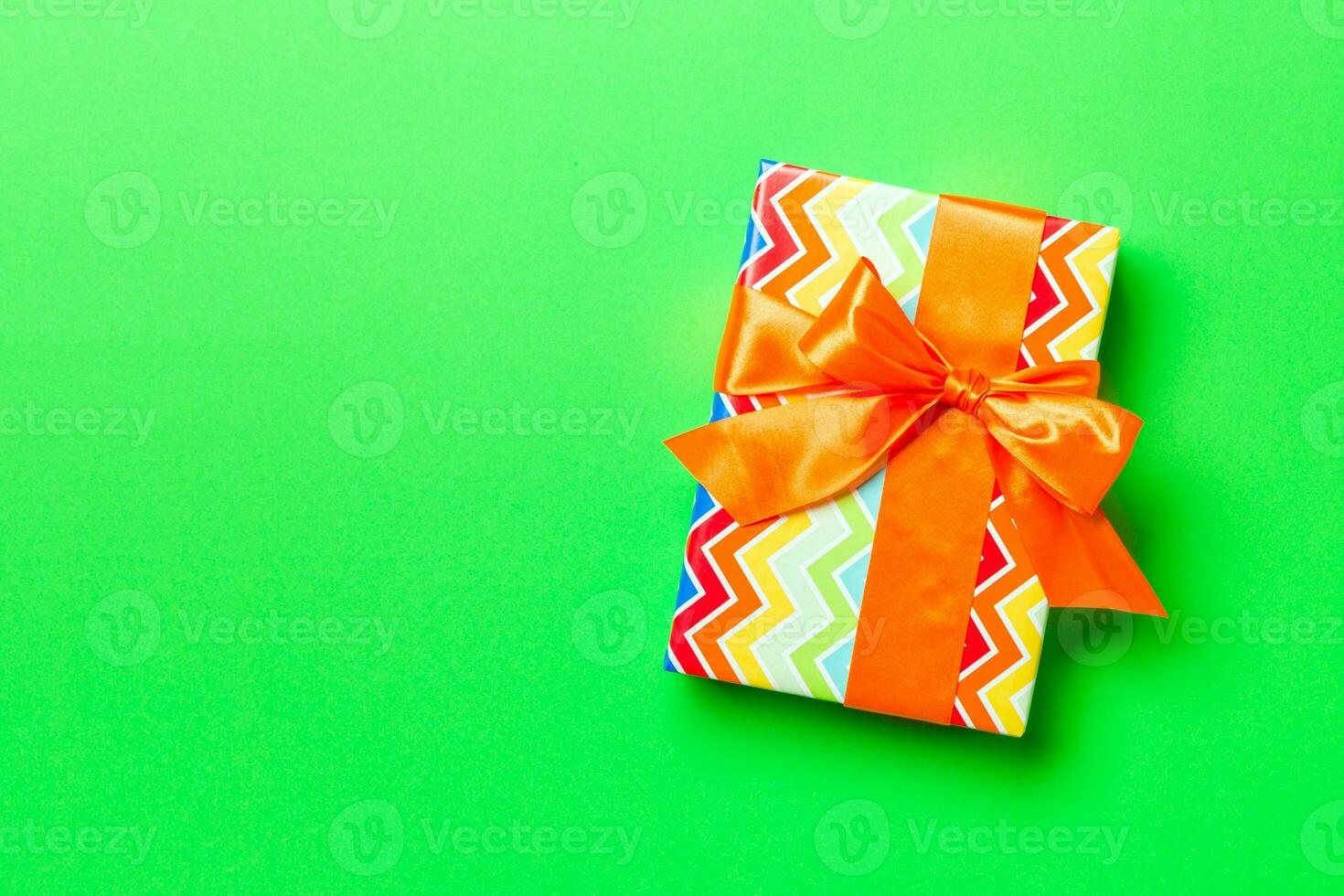 Top view Christmas present box with orange bow on green background with copy space photo