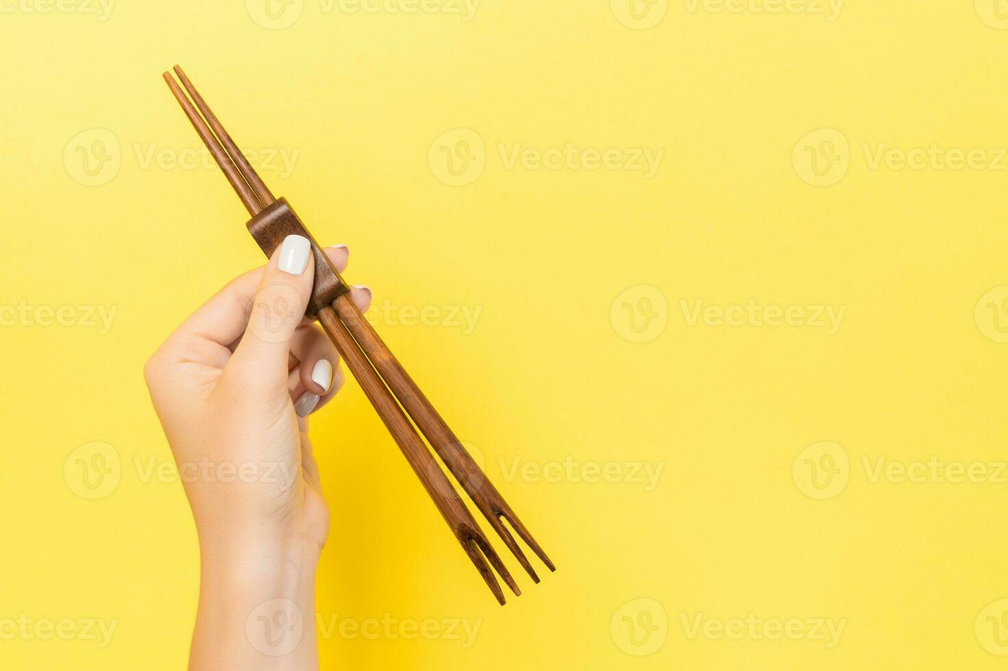 Female hand holding chopsticks on yellow background. Sushi concept with empty space for your idea photo