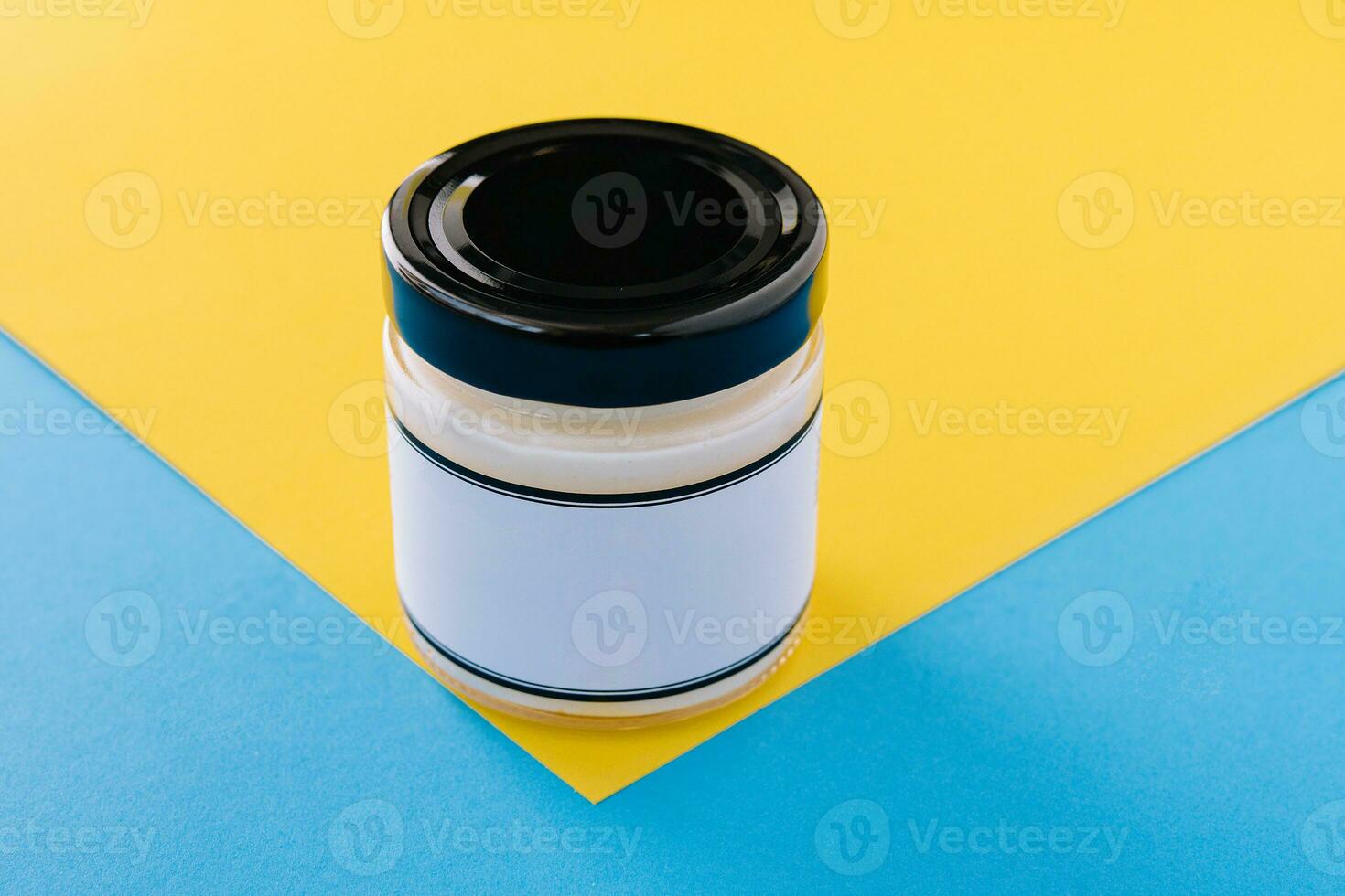 Glass mayonnaise jar with black lid on yellow photo