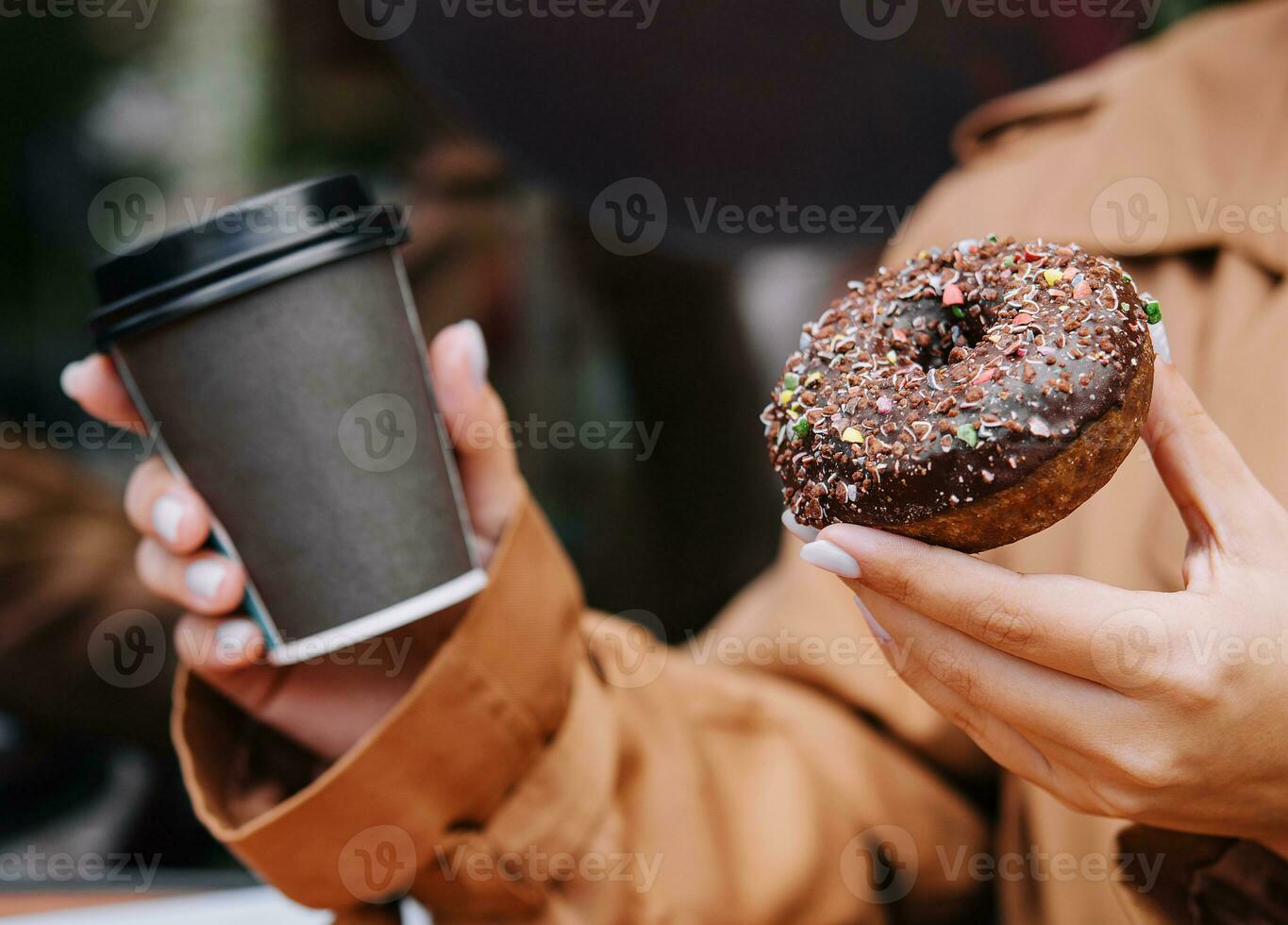 Female hands are holding a donut and a cup of coffee photo