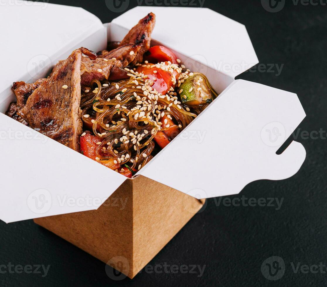 Close-up of noodles in a box with vegetables and beef in teriyaki sauce photo