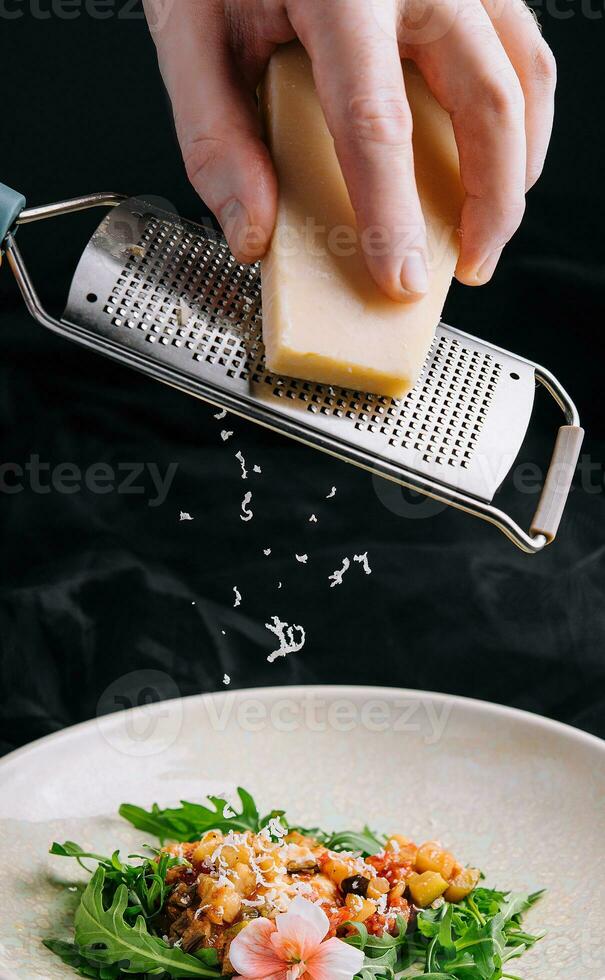 el proceso de Cocinando calentar ensalada. mano de el cocinar frota el queso en un rallador. foto