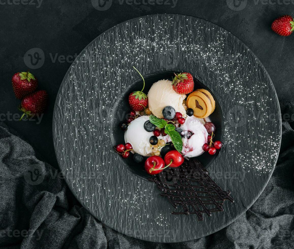 Vanilla ice cream scoops with fresh berries on black plate photo