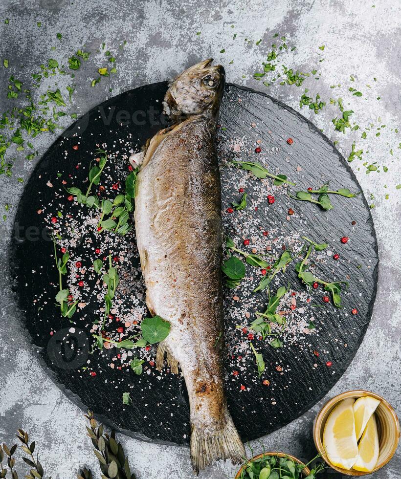 Grilled spicy fish on black plate, top view photo