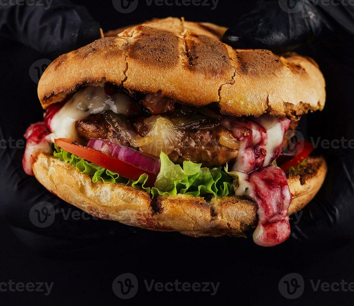 hombre sostiene Listo sabroso hamburguesa en manos en negro guantes foto