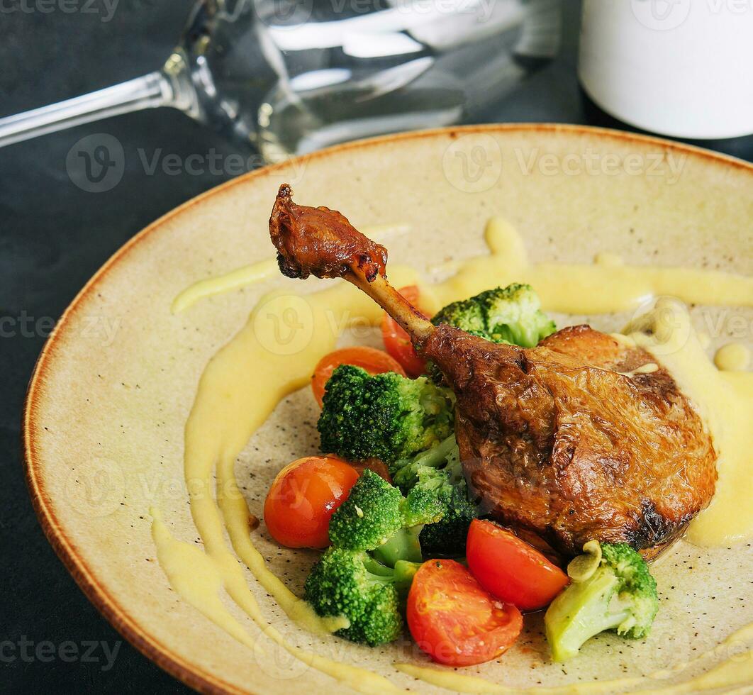 Confit duck leg with broccoli and tomatoes photo