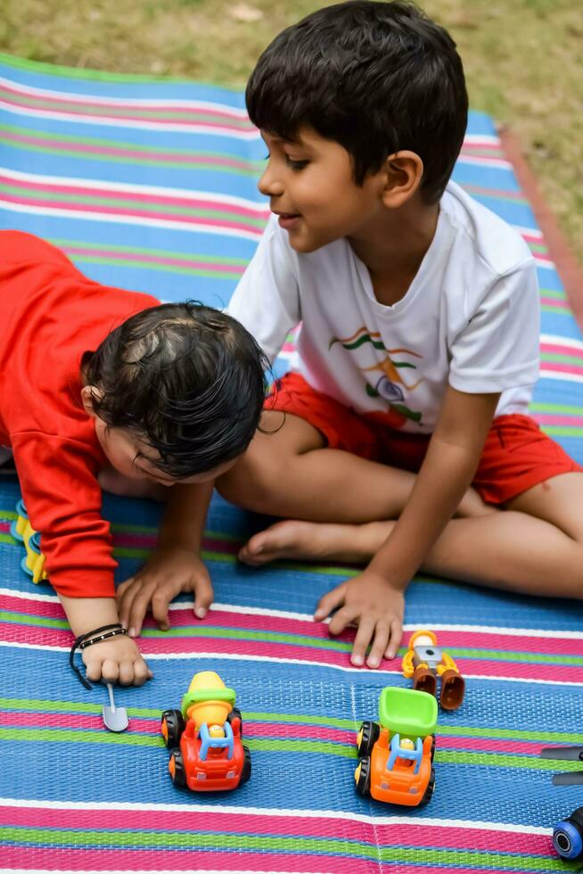 dos contento Niños en sociedad parque, contento asiático hermanos quien son sonriente felizmente juntos. hermanos jugar al aire libre en verano, mejor amigos. niñito bebé chico jugando con su contento hermano en el jardín foto