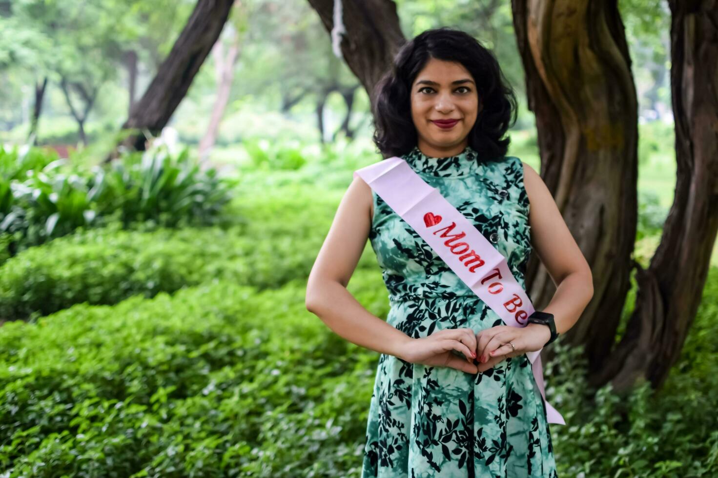 un embarazada indio dama poses para al aire libre el embarazo disparar y manos en barriga, indio embarazada mujer pone su mano en su estómago con un maternidad vestir a sociedad parque, embarazada fuera de maternidad disparar foto