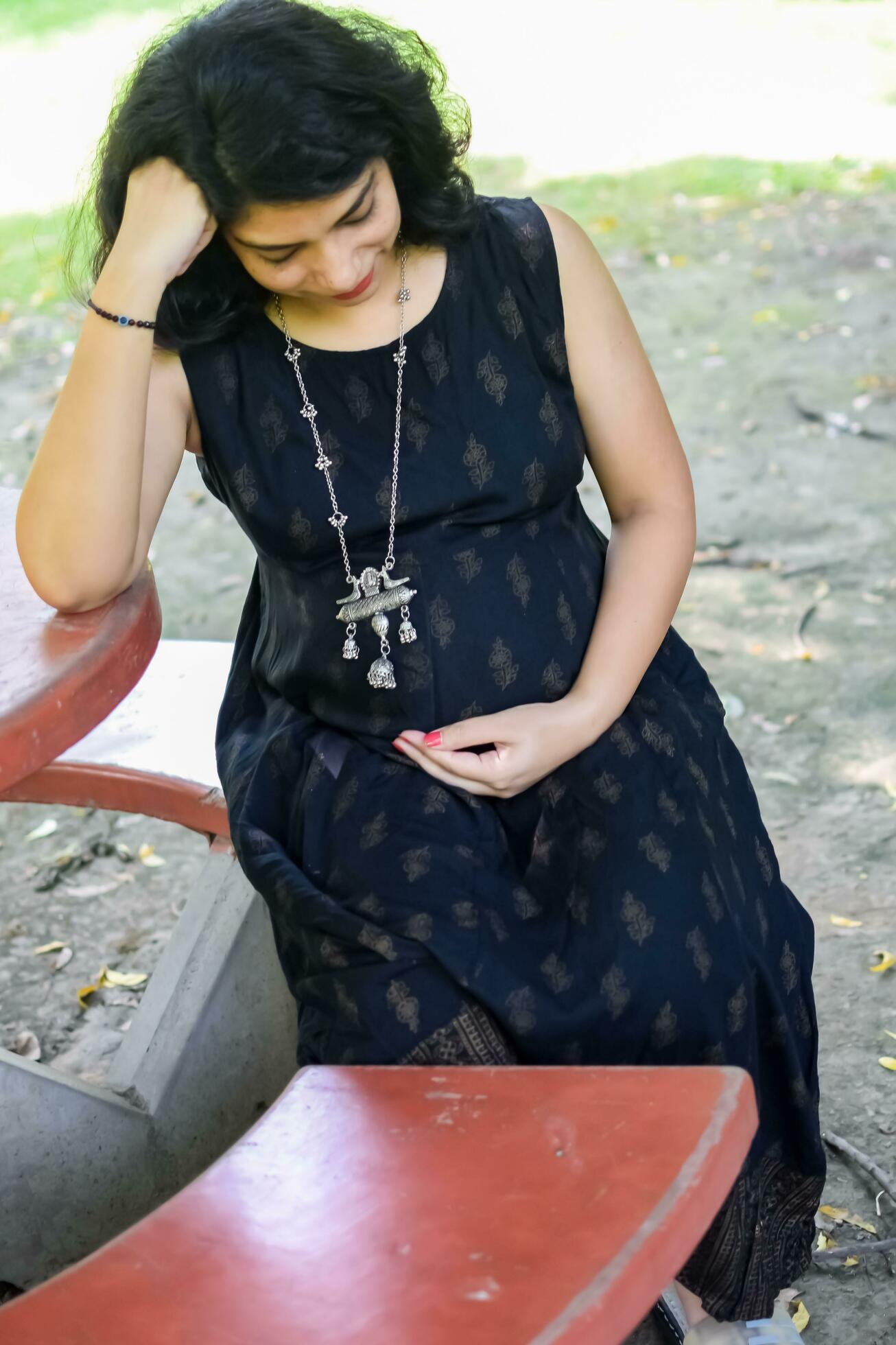 A pregnant Indian lady poses for outdoor pregnancy shoot and hands on belly,  Indian pregnant woman puts her hand on her stomach with a maternity dress  at society park, Pregnant outside maternity