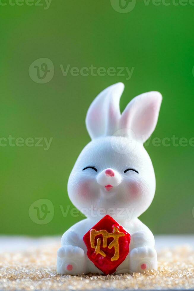 Three cute Chinese bunnies doll holding a red money bag and smile with green nature blurred background. Lovely rabbit character designs for Mid Autumn Festival, Year of the rabbit 2023, and Easter photo