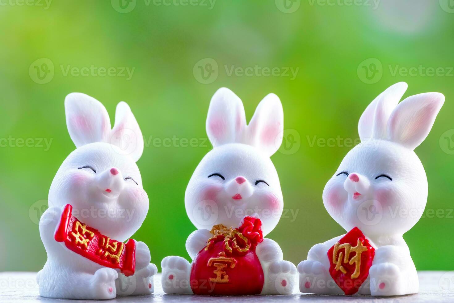 Three cute Chinese bunnies doll holding a red money bag and smile with green nature blurred background. Lovely rabbit character designs for Mid Autumn Festival, Year of the rabbit 2023, and Easter photo