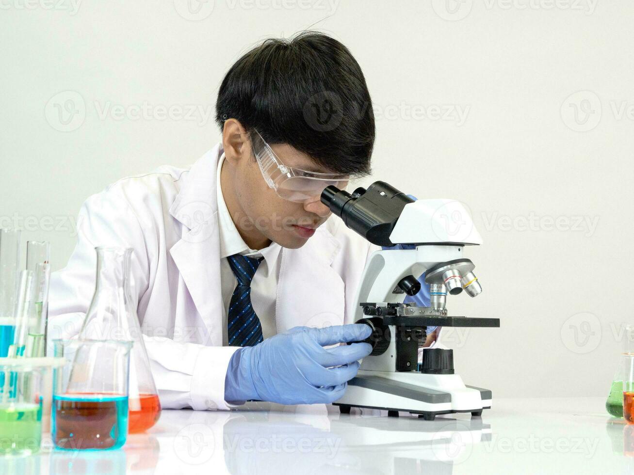 retrato asiático hombre estudiante científico vistiendo un médico vestido en el laboratorio mirando mano a químico. causado por mezcla reactivos en científico investigación laboratorios con prueba tubos y microscopio en el mesa foto