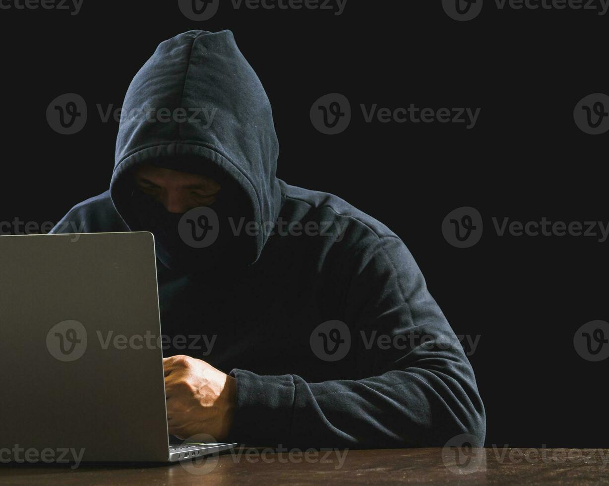 Hacker spy man one person in black hoodie sitting on a table looking computer laptop used login password attack security to circulate data digital in internet network system, night dark background. photo