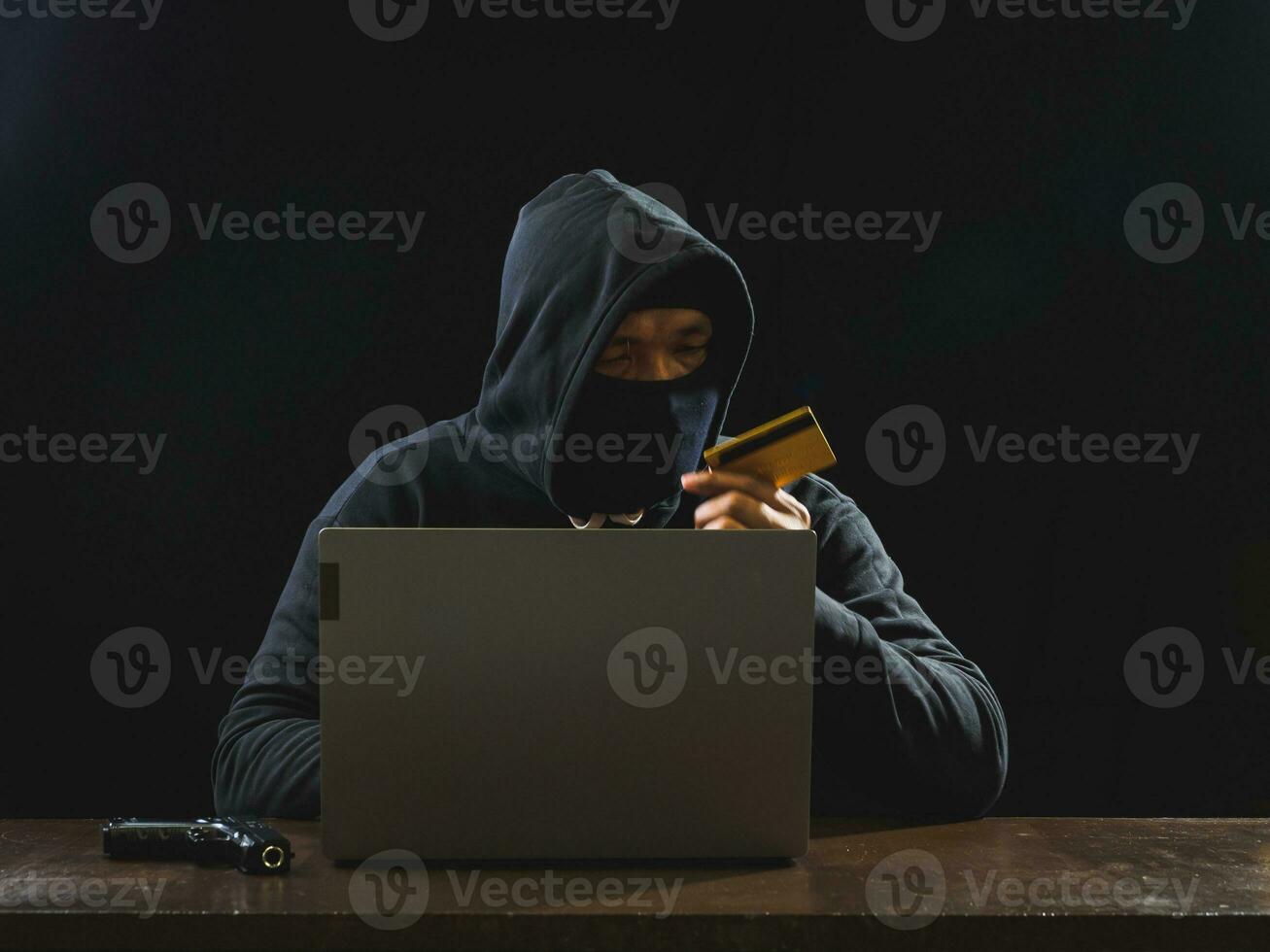 Hacker spy man one person in black hoodie sitting on a table looking computer laptop used login password attack security to circulate data digital in internet network system, night dark background. photo