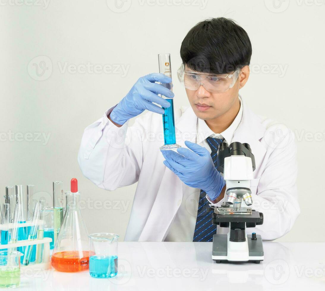 retrato asiático hombre estudiante científico vistiendo un médico vestido en el laboratorio mirando mano a químico. causado por mezcla reactivos en científico investigación laboratorios con prueba tubos y microscopio en el mesa foto