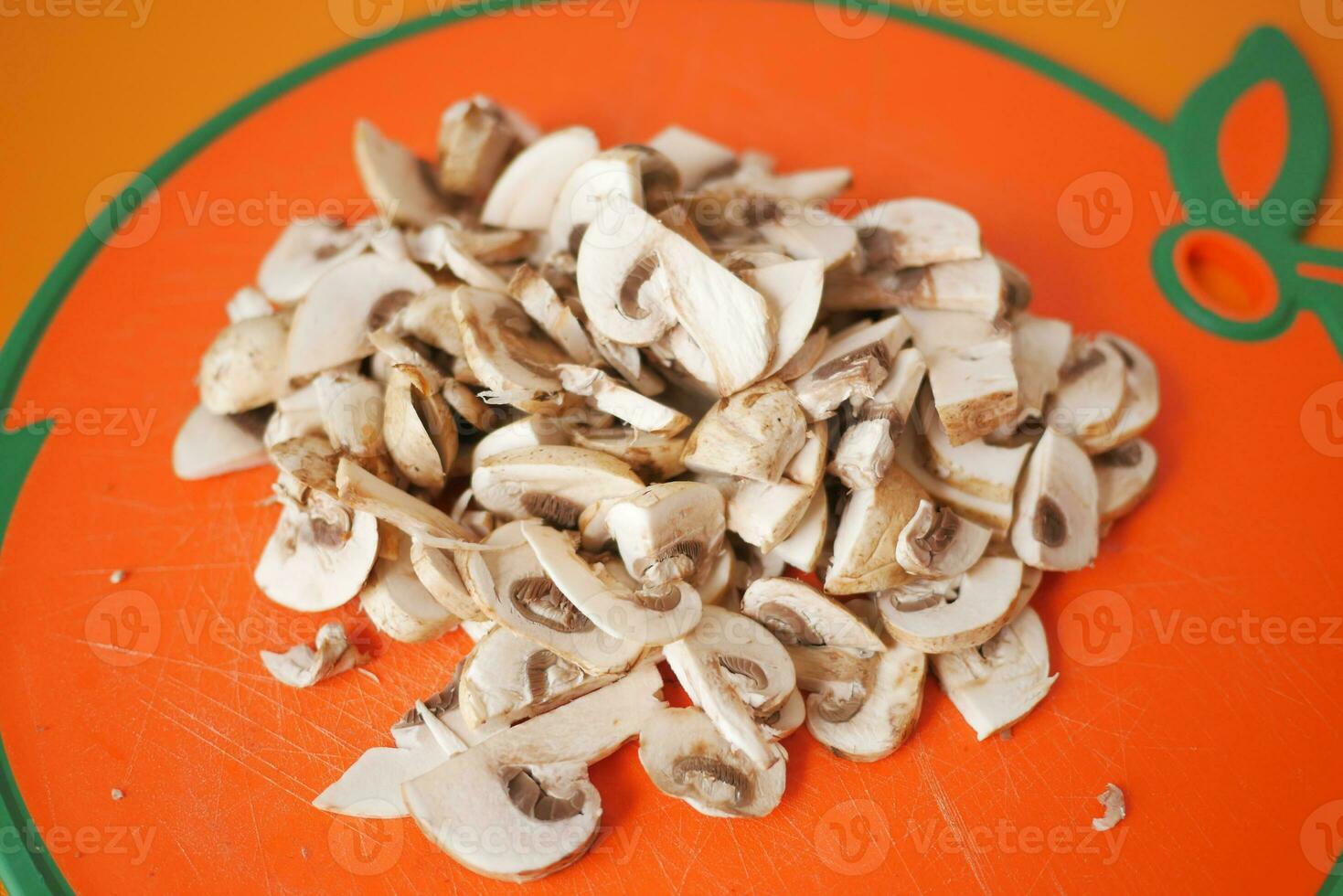 Sliced champignon mushrooms on a chopping board on orange background photo