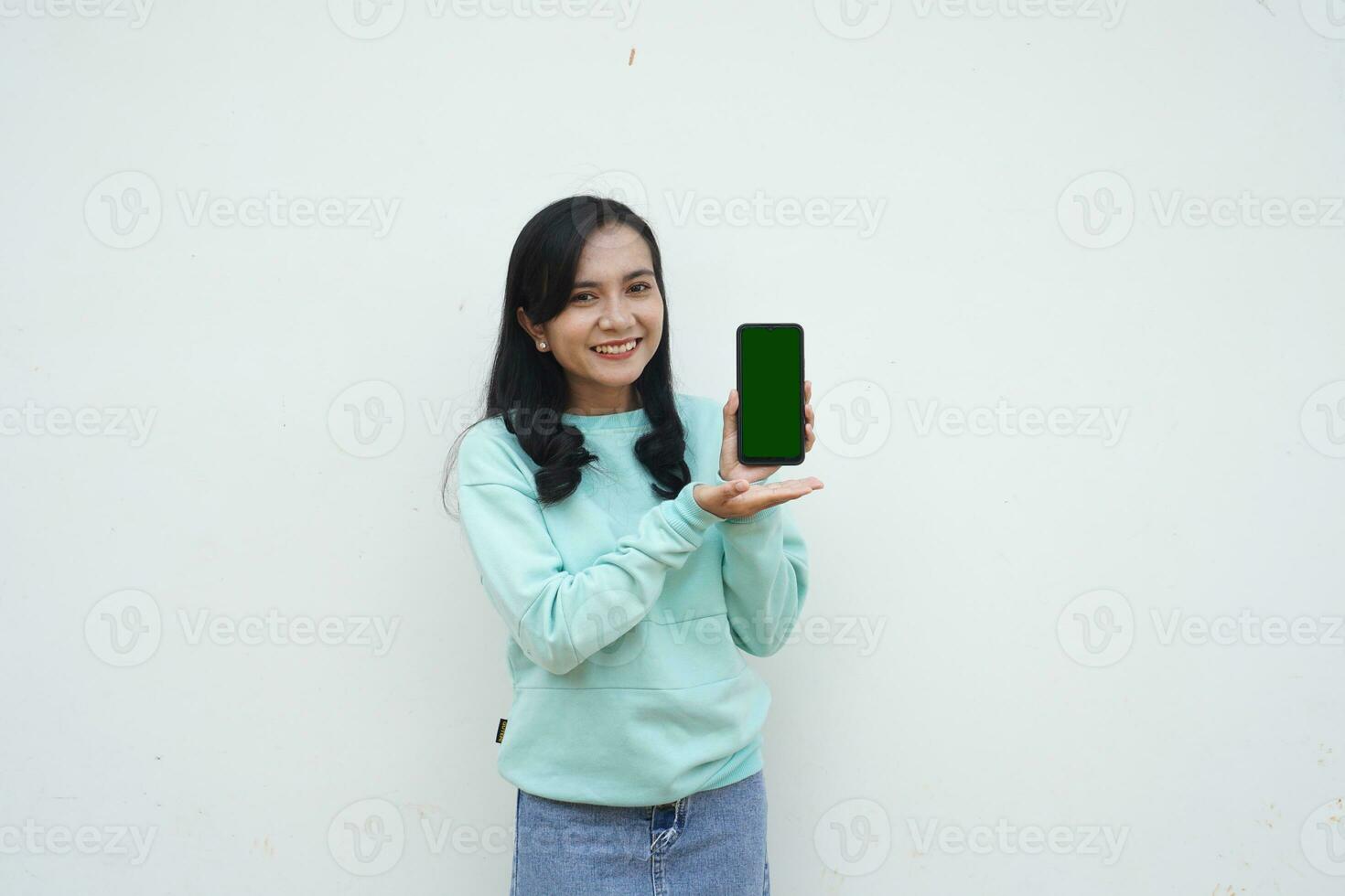 Portrait Indonesian beautiful woman wearing light blue sweater with happy and smile face show green screen mobile phone isolated on white background photo