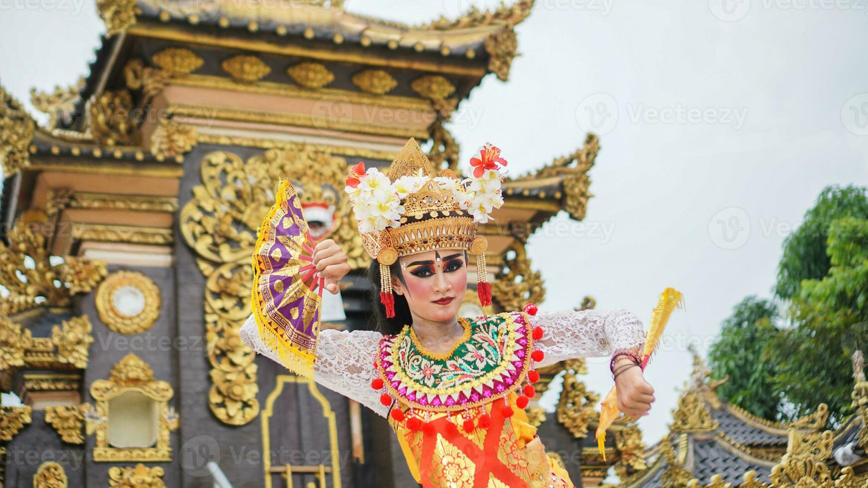 niña vistiendo balinés tradicional vestir con un bailando gesto en balinés templo antecedentes con Mano admirador, corona, joyas, y oro ornamento accesorios. balinés bailarín mujer retrato foto