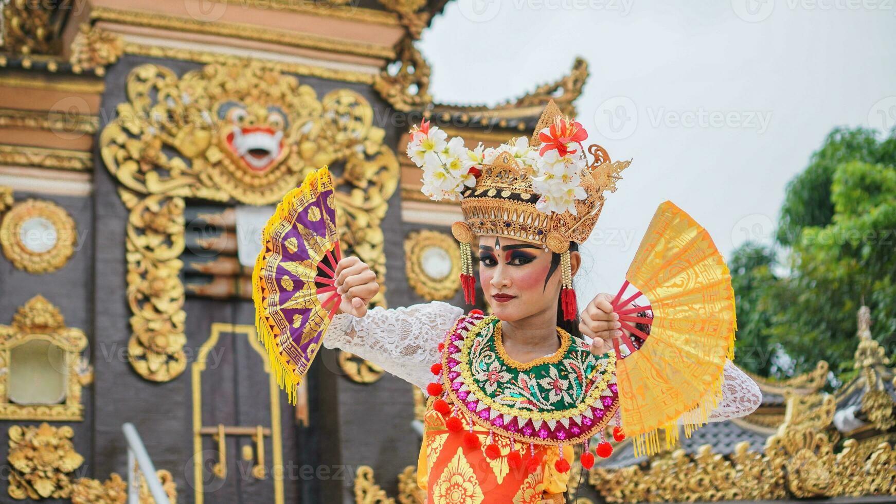 niña vistiendo balinés tradicional vestir con un bailando gesto en balinés templo antecedentes con Mano admirador, corona, joyas, y oro ornamento accesorios. balinés bailarín mujer retrato foto