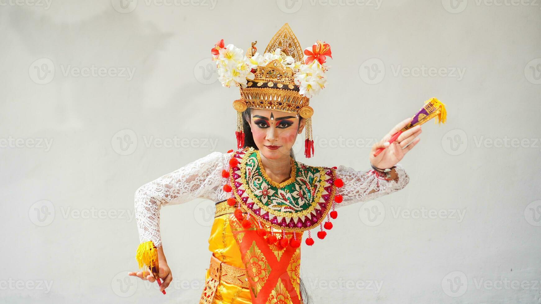 girl wearing Balinese traditional dress with a dancing gesture on white background with hand-held fan, crown, jewelry, and gold ornament accessories. Isolated Balinese dancer woman portrait photo