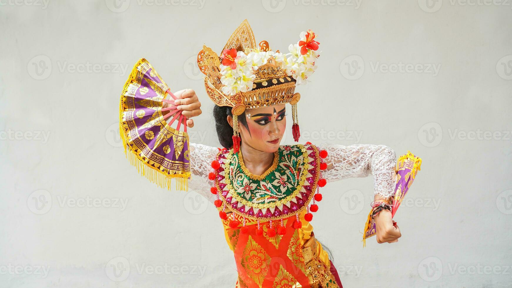 girl wearing Balinese traditional dress with a dancing gesture on white background with hand-held fan, crown, jewelry, and gold ornament accessories. Isolated Balinese dancer woman portrait photo