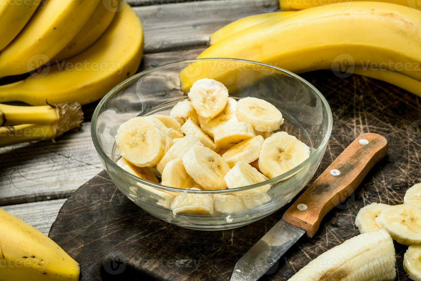 Bananas and banana slices in a plate on a black chopping Board with a knife. photo