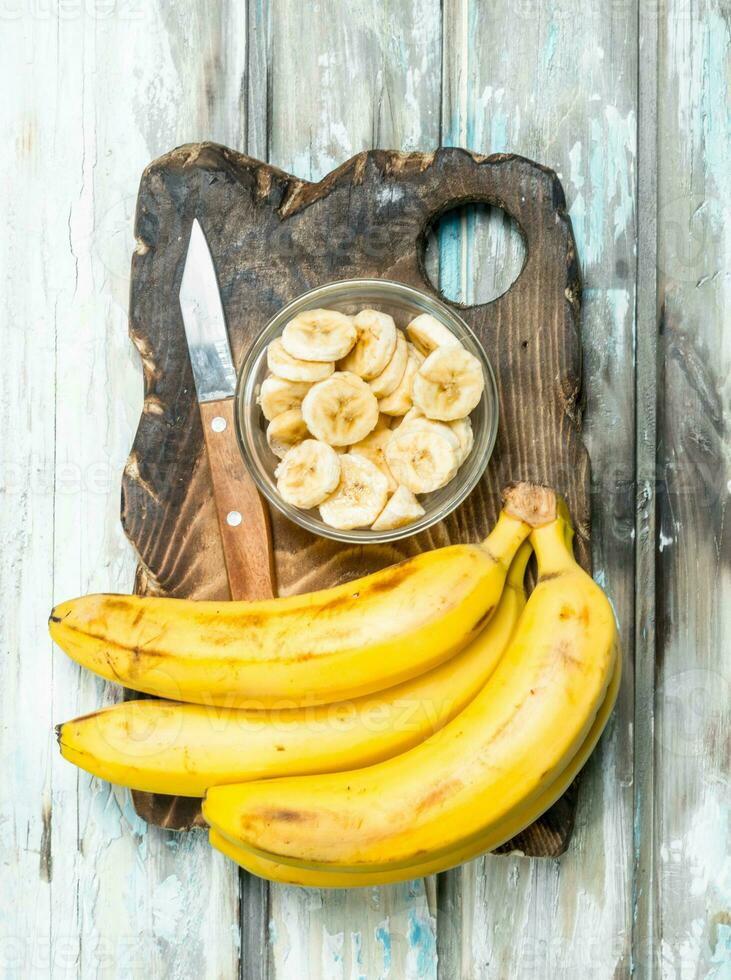 Bananas and banana slices in a glass bowl on an old cutting Board. photo