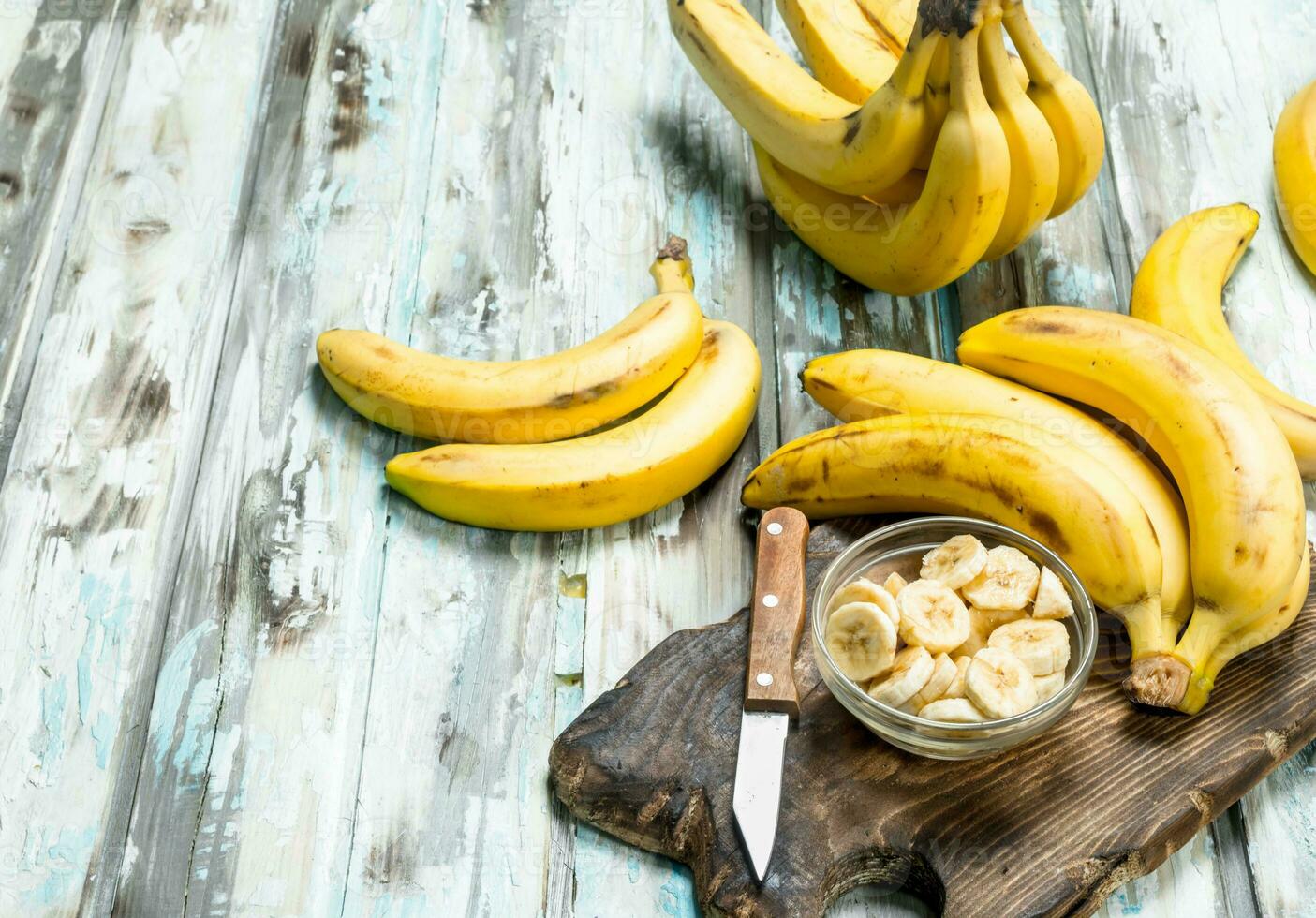 Bananas and banana slices in a glass bowl on an old cutting Board. photo