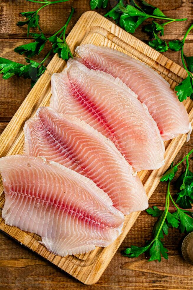 Raw fish fillet with parsley on a cutting board. photo
