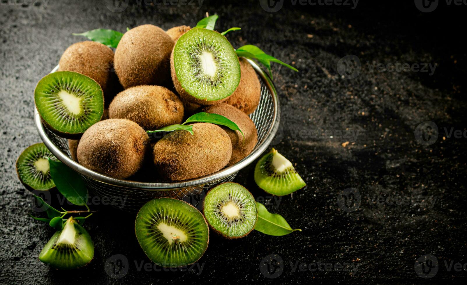 Ripe kiwi with leaves in a colander on the table. photo